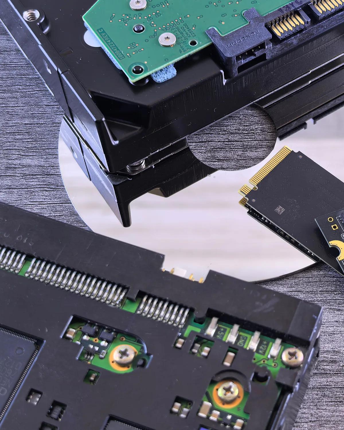 A hard drive, an optical disc and solid state drives laid out on a desk, the copies a backup lives on.