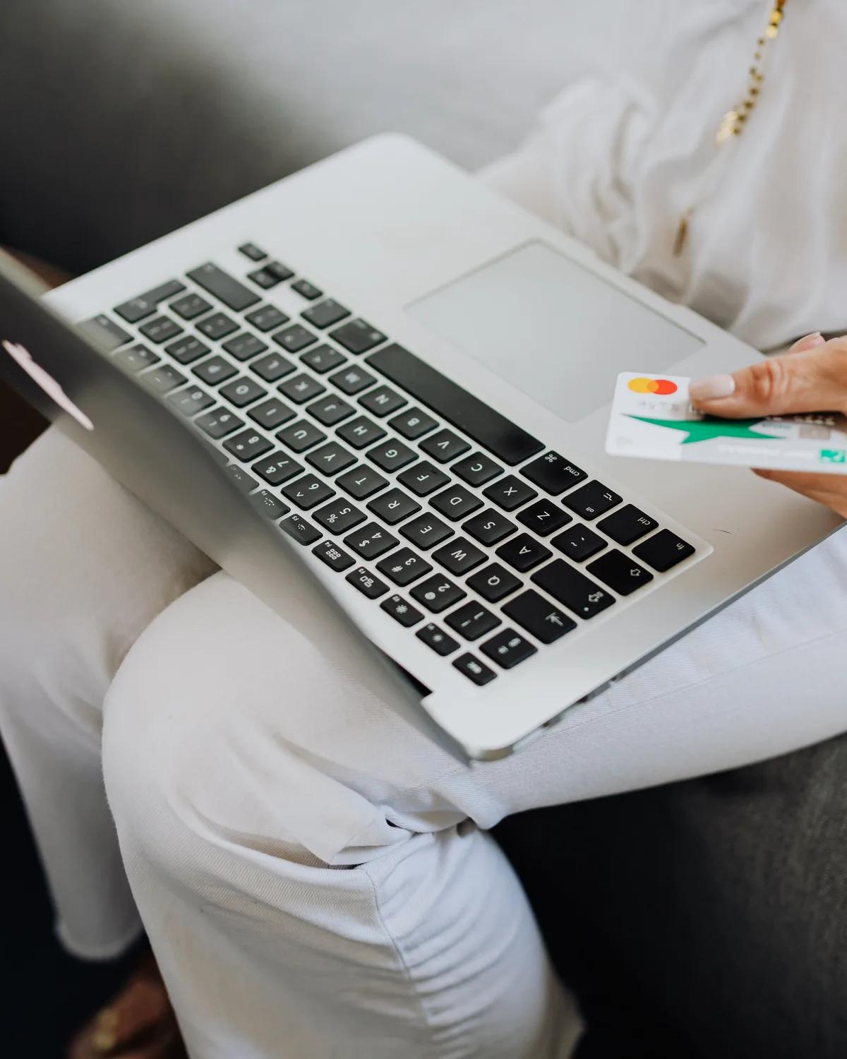 A shopper on a sofa holding a bank card beside a laptop, paying for an order.
