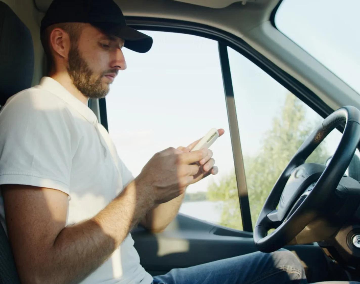 A tradesman in a van cab checking a job on his phone.